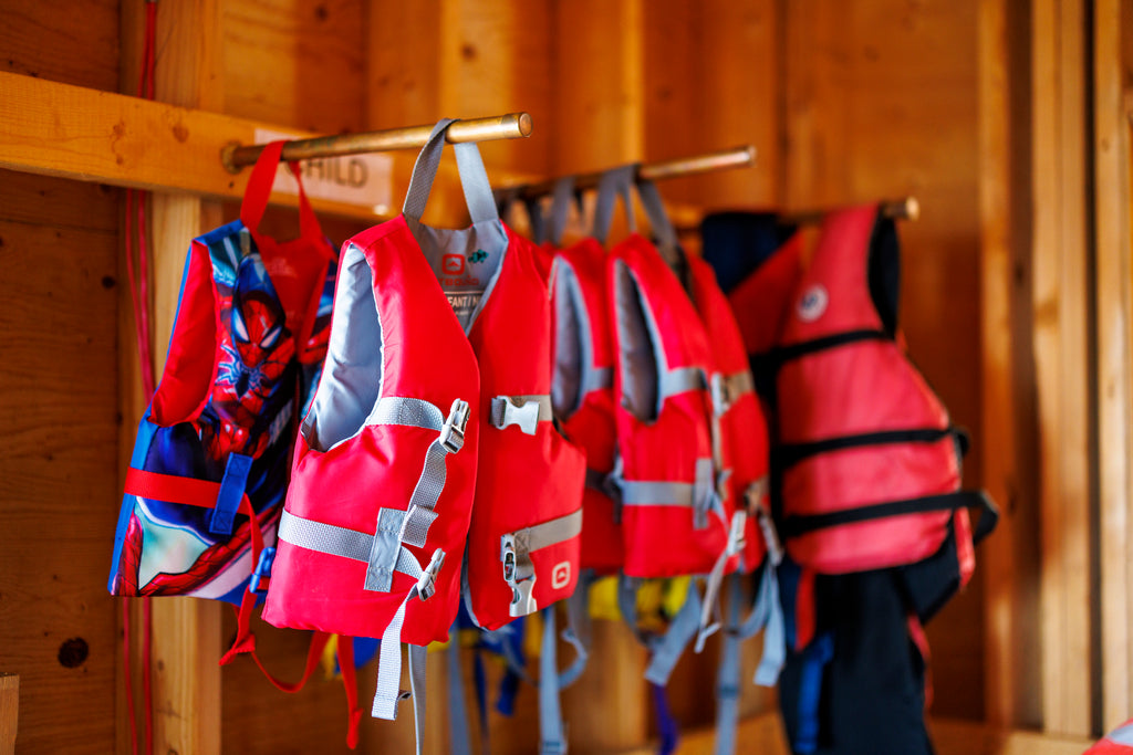 Red life jackets hang from metal hooks mounted on a wooden wall.