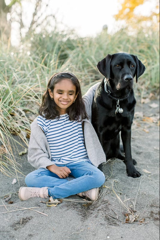 A smiling child sits with her arm around her CNIB Buddy Dog. 