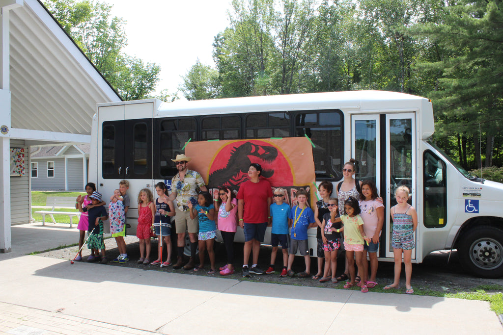 A large group of children with sight loss stand in front of an accessible bus. 